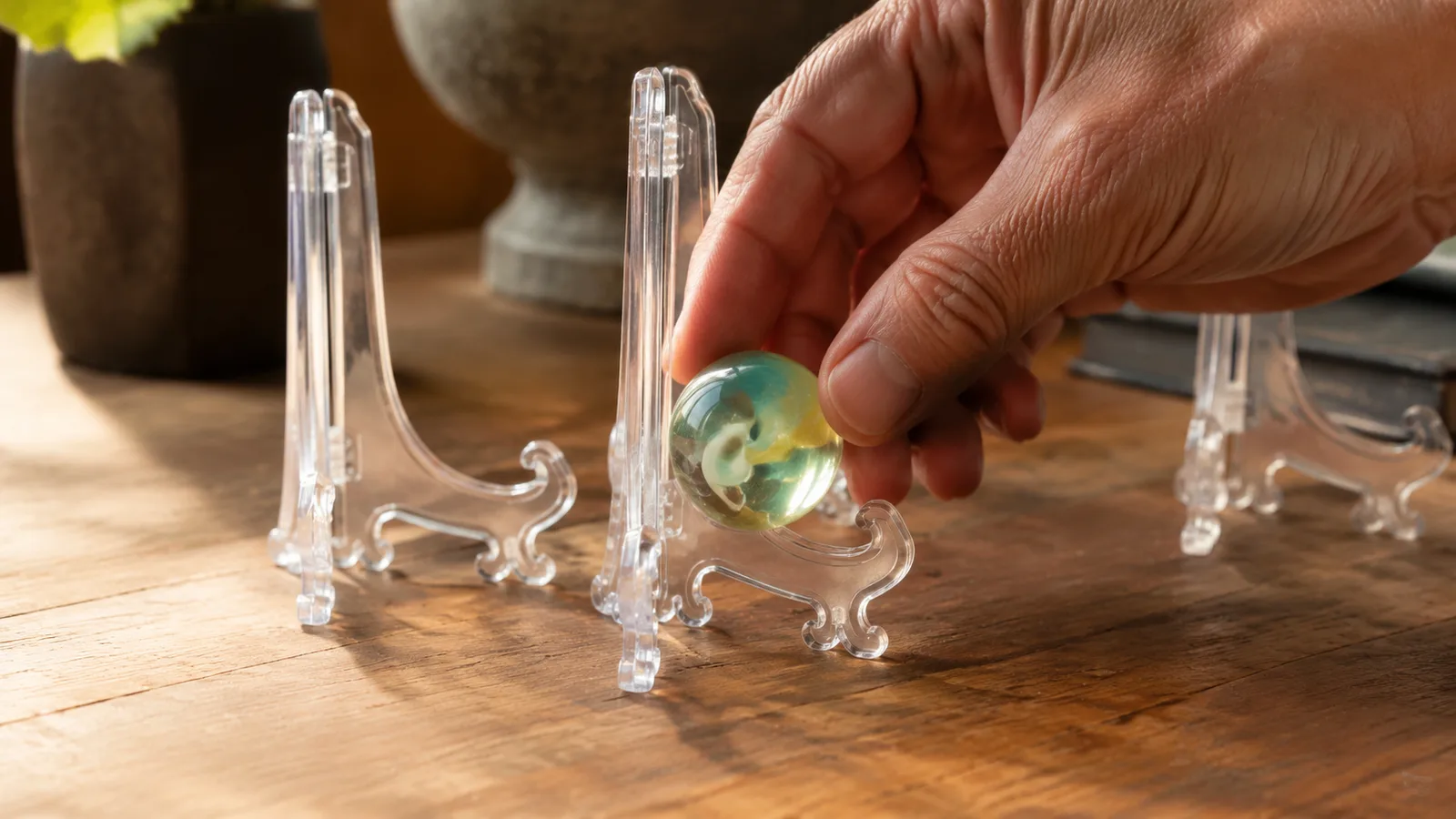 A hand placing one marble onto a small clear acrylic easel stand on a table