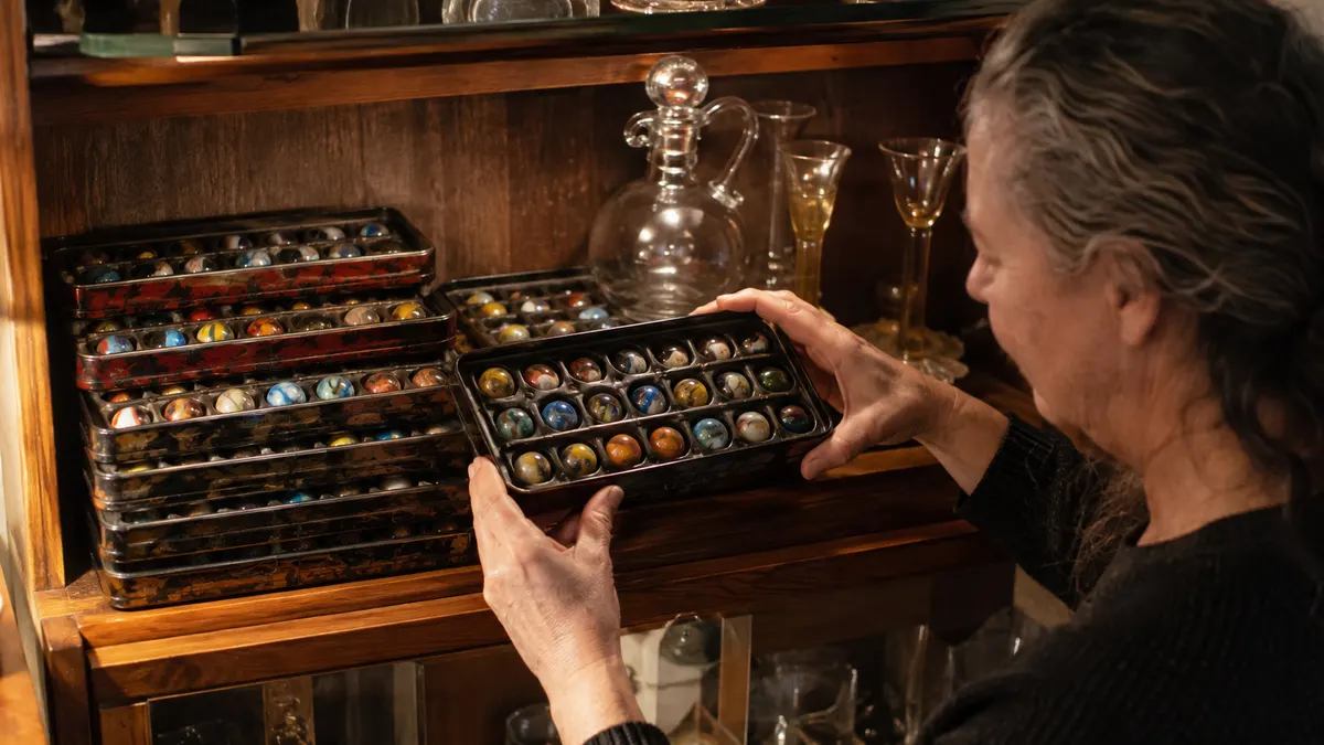 Three flat marble tins stacked neatly beside glassware in a wooden display cabinet, dust-free under a soft light
