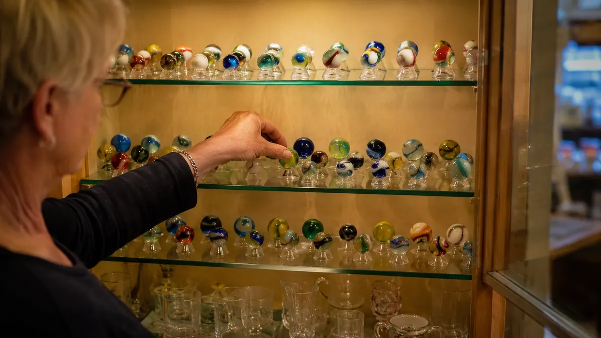 A glass-fronted display cabinet holding rows of marbles on clear acrylic stands, lit from within