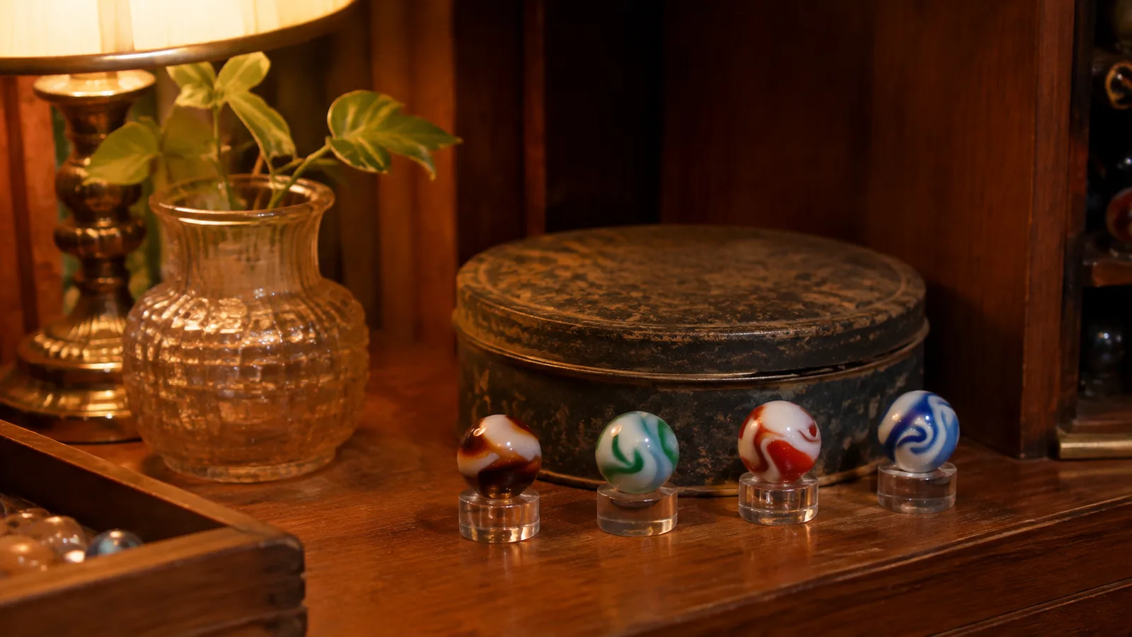 A shelf where a few best marbles from a tin stand on clear acrylic holders beside the closed tin box
