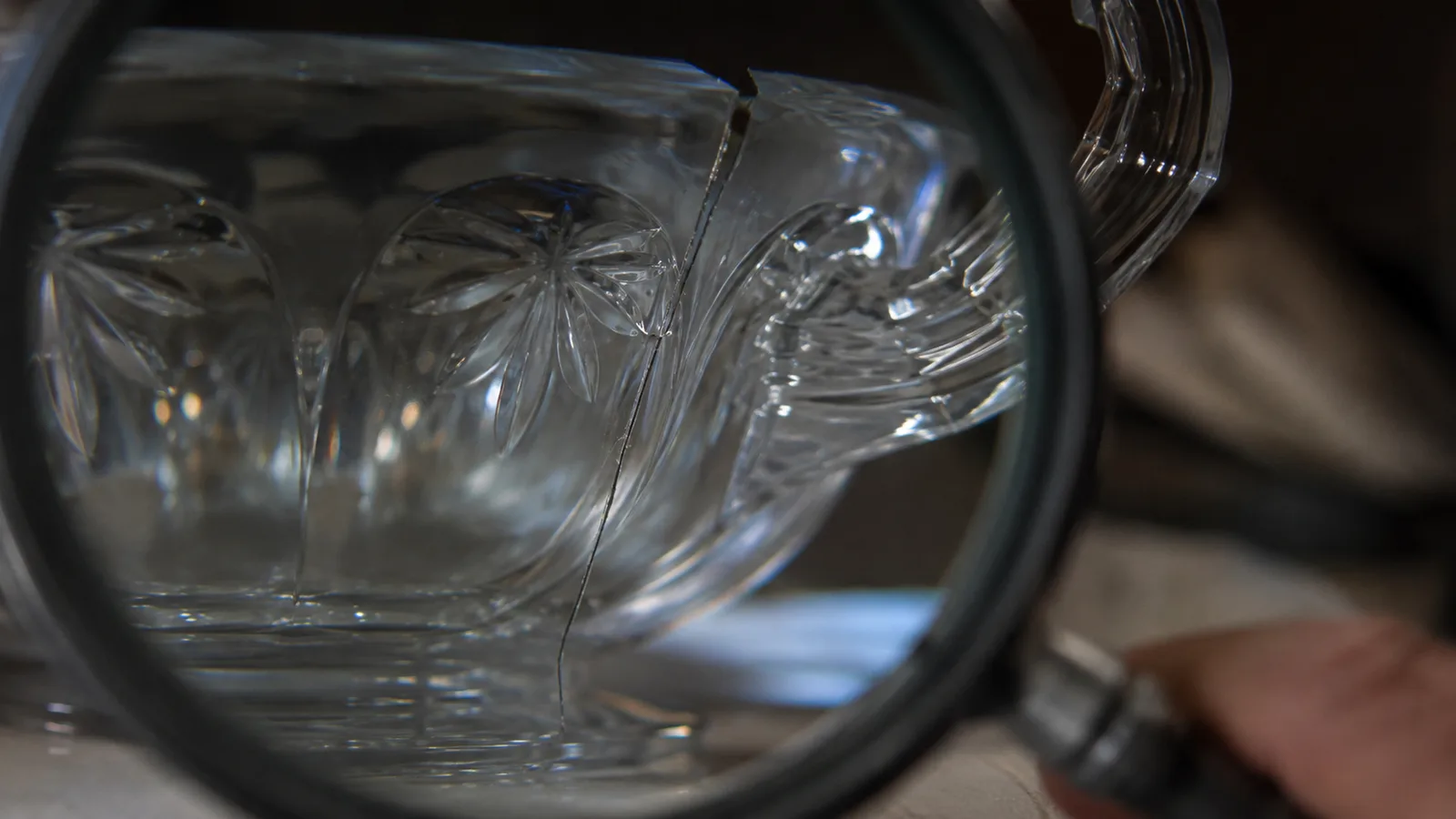 A macro close-up of a hairline crack running up the cut base of a glass bowl handle, visible only under magnification