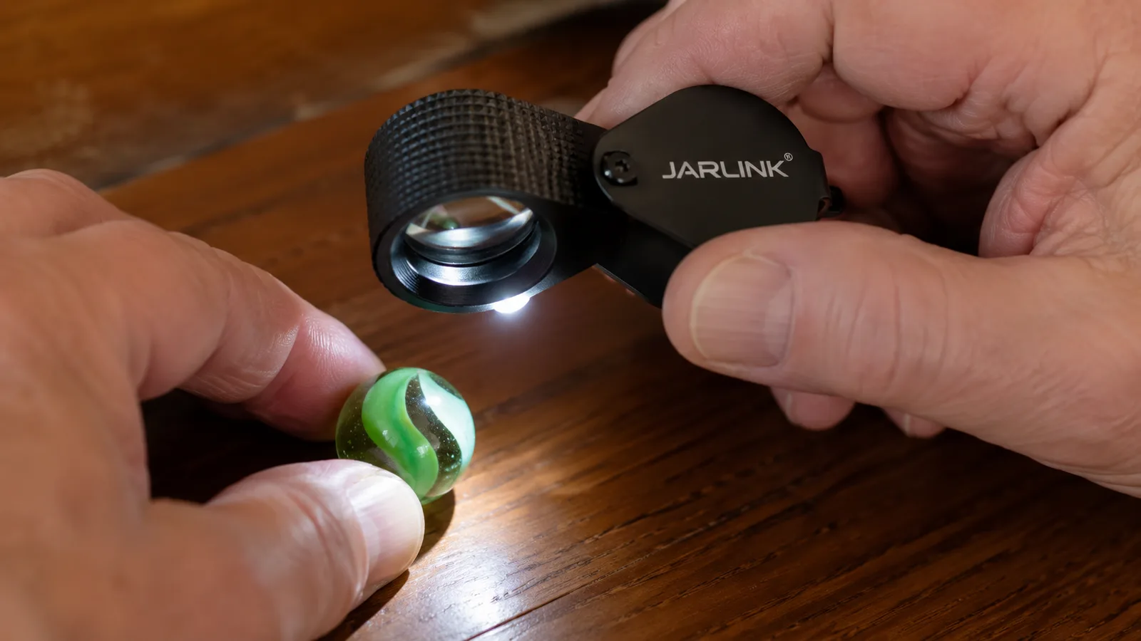A hand holding an illuminated jeweler's loupe an inch from a glass marble to inspect its surface